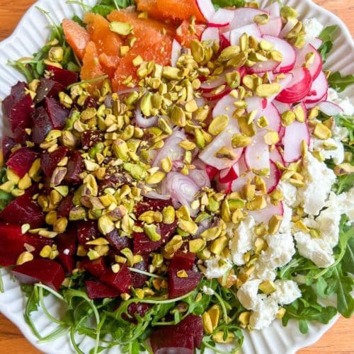 Arugula Salad with Beets, Goat Cheese and Pistachios set on a wooden table