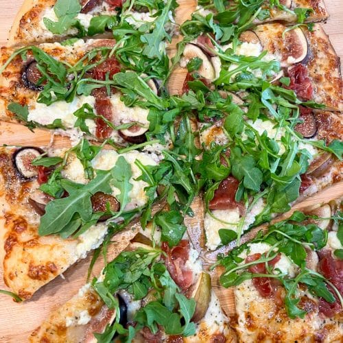 Fig and prosciutto pizza with arugula and hot honey cut into slices