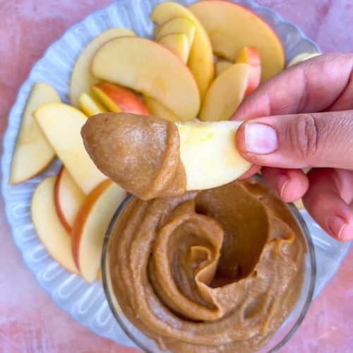 A person dipping an apple slice into date caramel