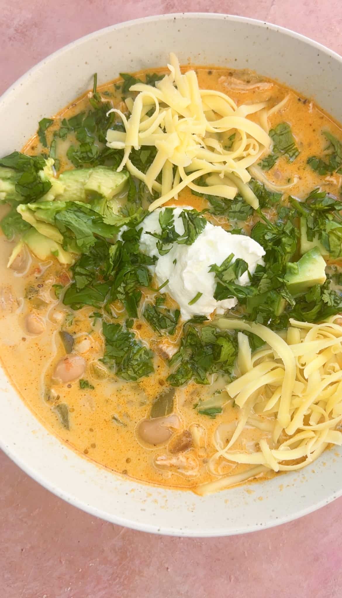 A bowl of easy creamy white chicken chili with toppings like yogurt, cilantro, avocado and shredded cheese