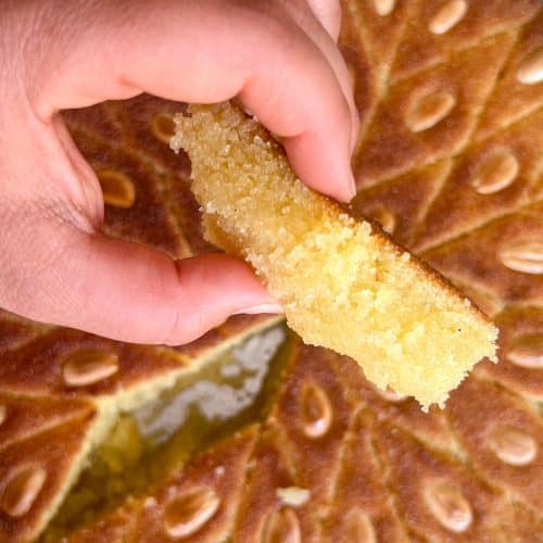 Someone holding a piece of basbousa above the tray